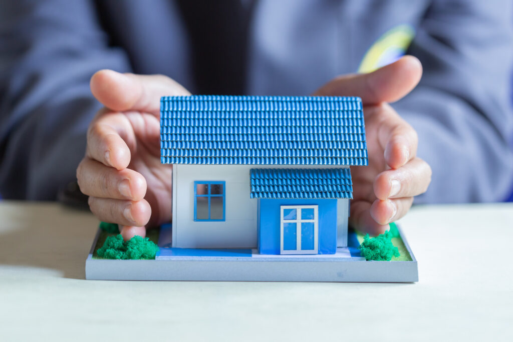 Hands protect a miniature blue-roofed house model.